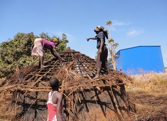 Women of Awoo Village in Karuma trying to remove some of the building materials from their huts as they are being evicted. Photographer unknown.